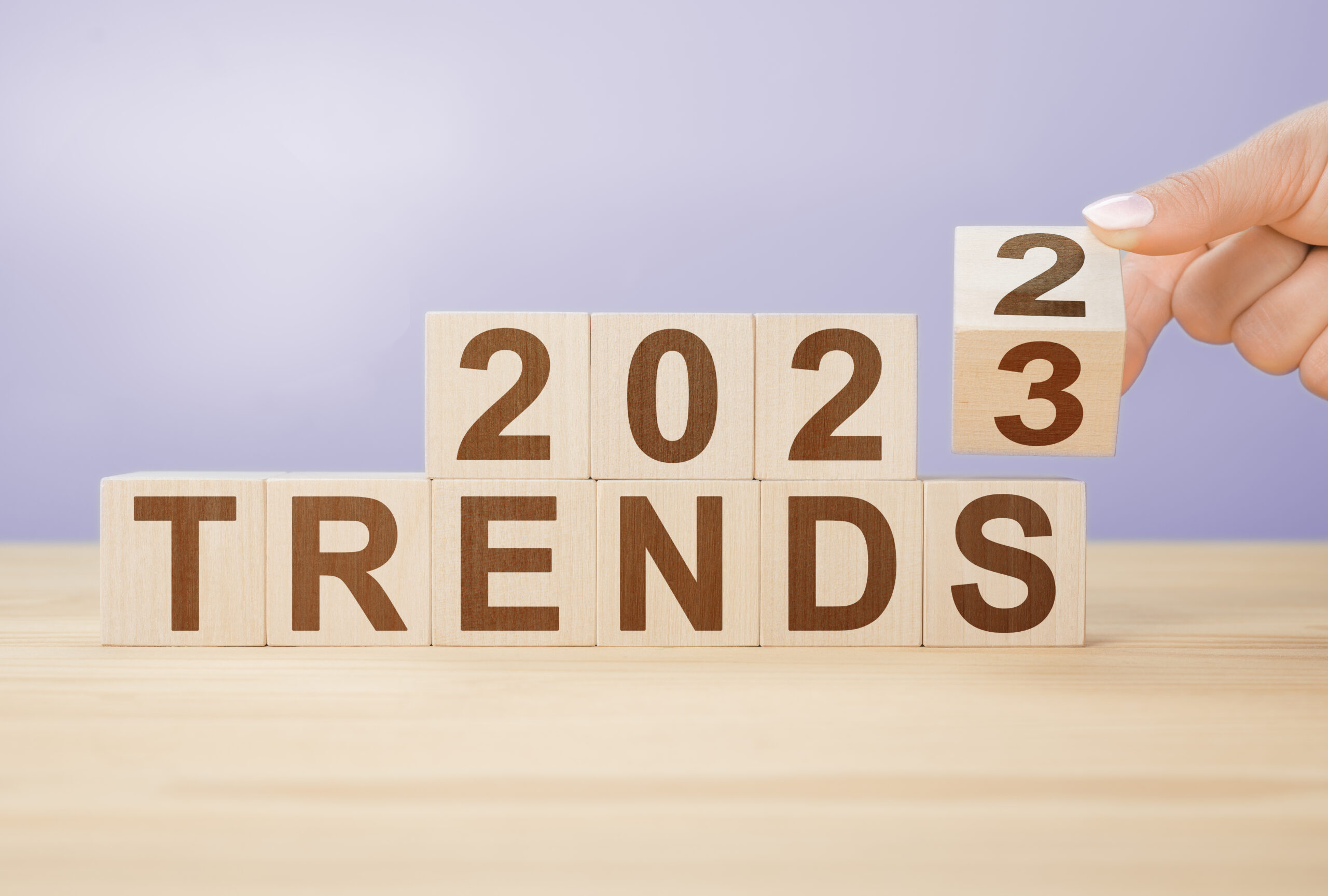 Businesswoman turns wooden cube and changes words 2022 to 20223 on very peri color background. Flipping of wooden cube block for change 2022 to 2023 year