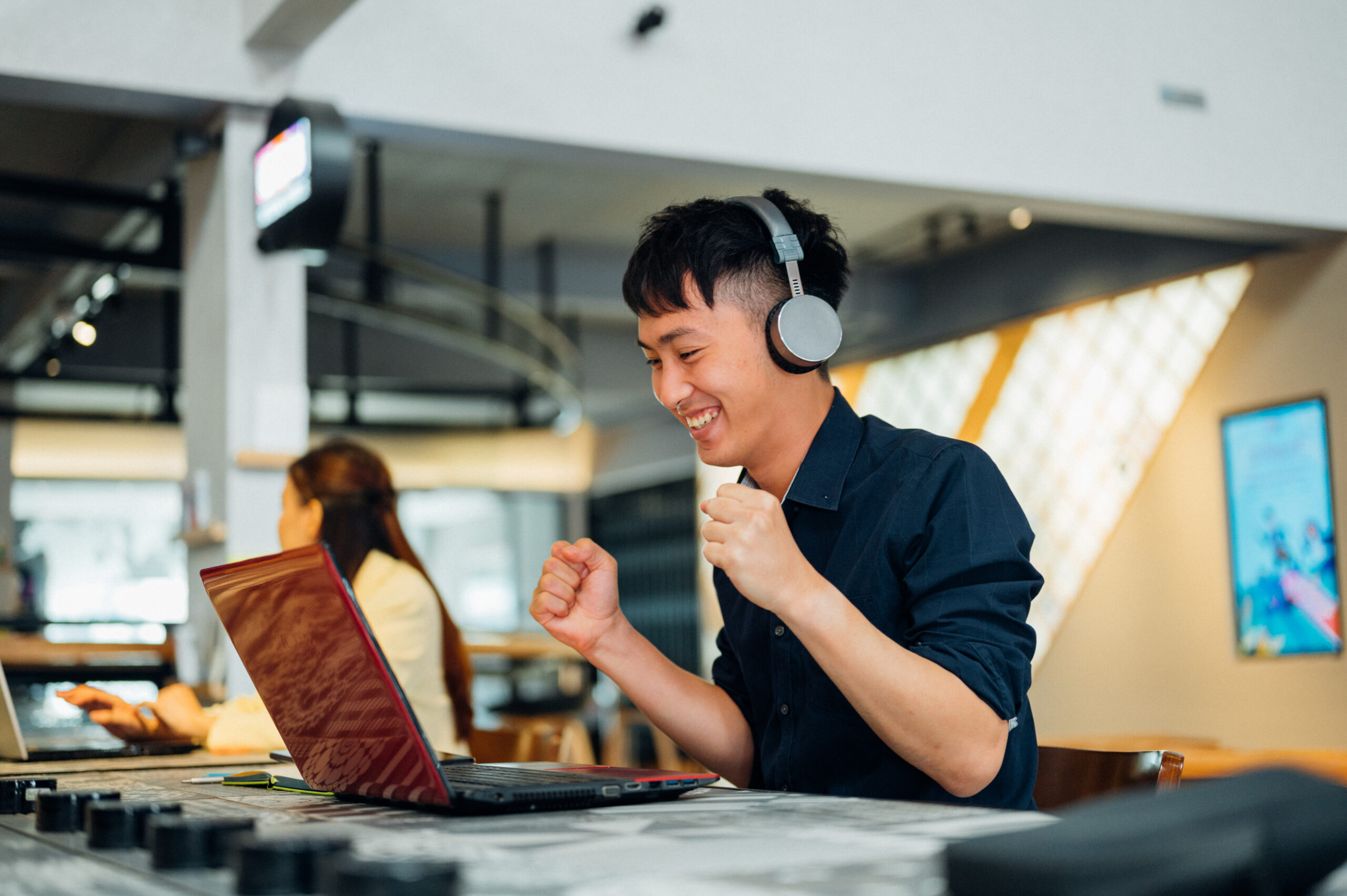 Happy Asian business man wearing headphones, enjoying watching educational webinar on laptop. Smiling young Asian businessman holding video call with clients partners.